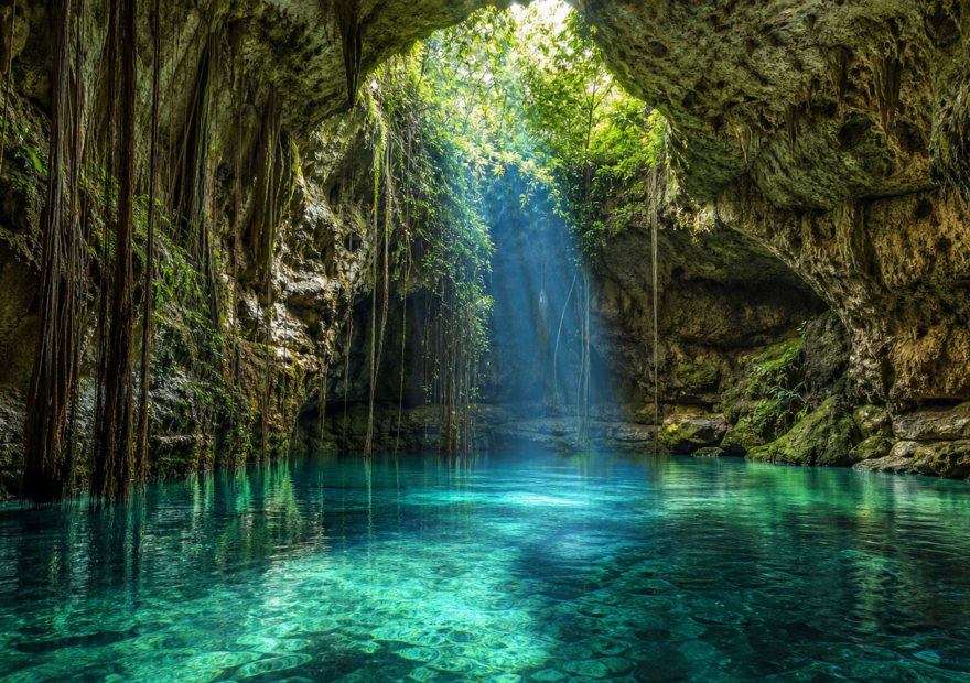 Cenote de agua turquesa entre rocas calizas y raíces en Yucatán