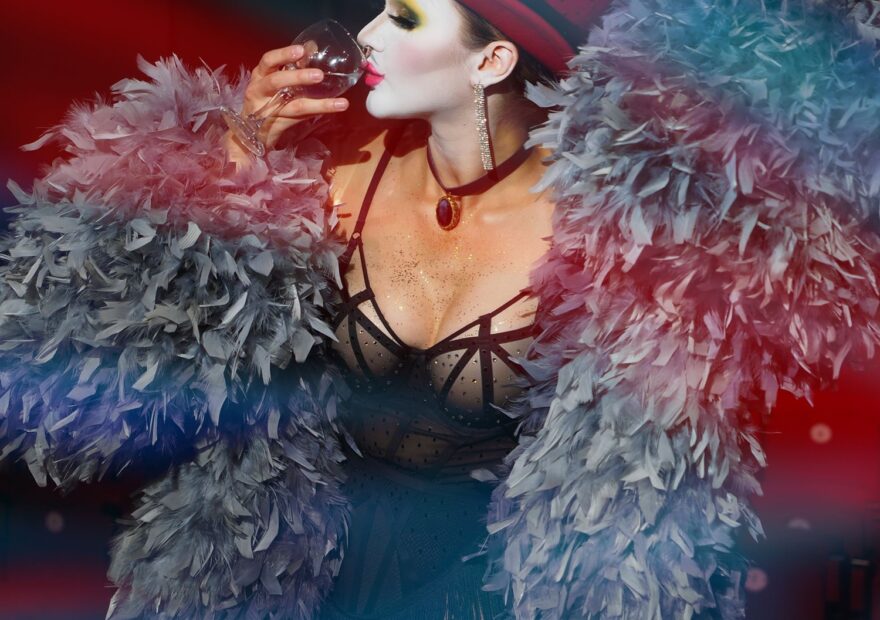 Imagen ilustrativa: artista en un espectáculo con vestuario de plumas y luces teatrales; no identifica un recinto cultural específico.