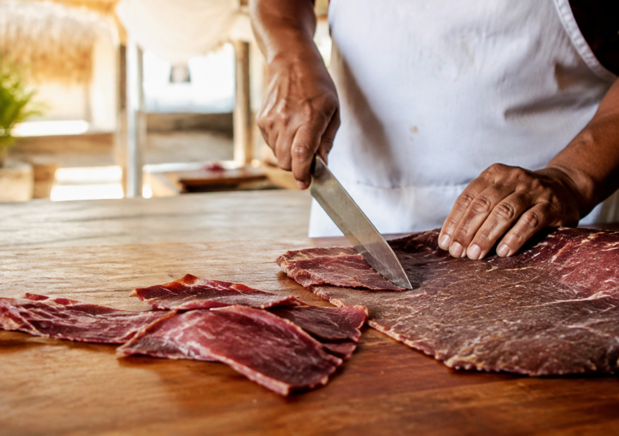 Maestro tasajeador corta cecina artesanal de Yecapixtla sobre una mesa de madera